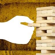 an in progress jenga game showing how all of the pieces are built upon each other. A hand starts to put on one piece watching to see if the stack falls,,, creating imagery of the assumption stack.