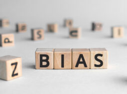 A white background with scrabble tiles spread across a table with four tiles put together to form the word "BIAS"