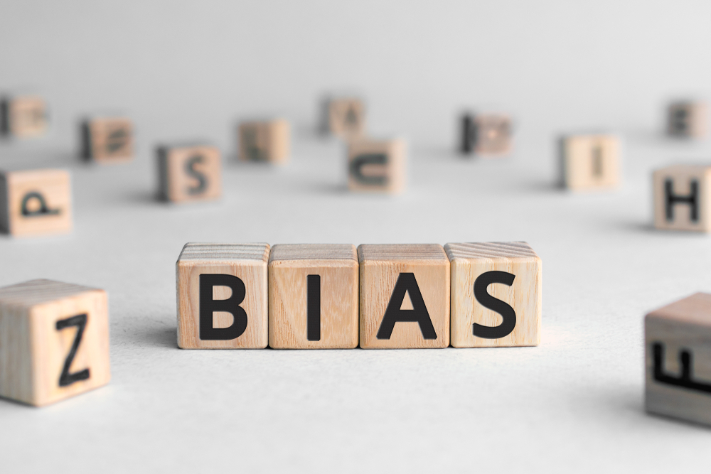A white background with scrabble tiles spread across a table with four tiles put together to form the word "BIAS"