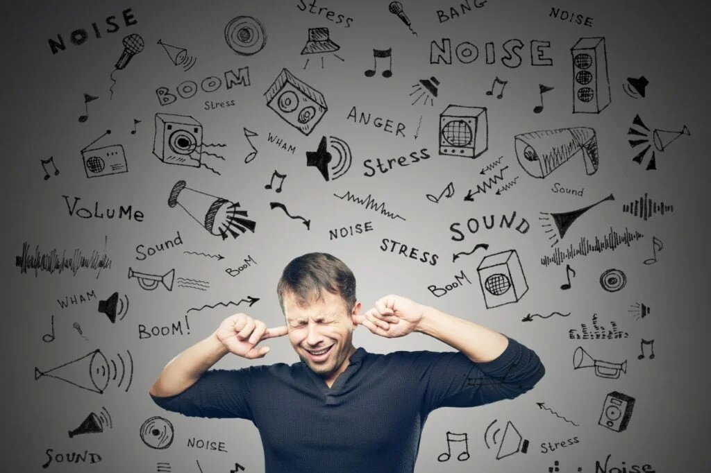 a man standing with his fingers in his ears to stop the influx of information . The source of the information is written on a white wall behind him. It illustrates the noise problem when trying to focus.